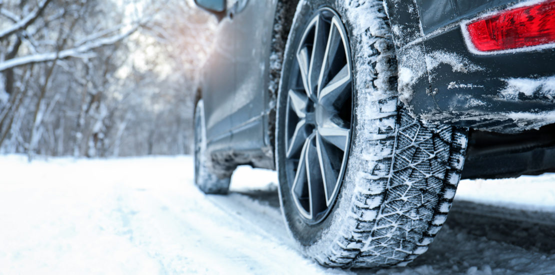 Winter tires on a snowy country road with car on winter day.